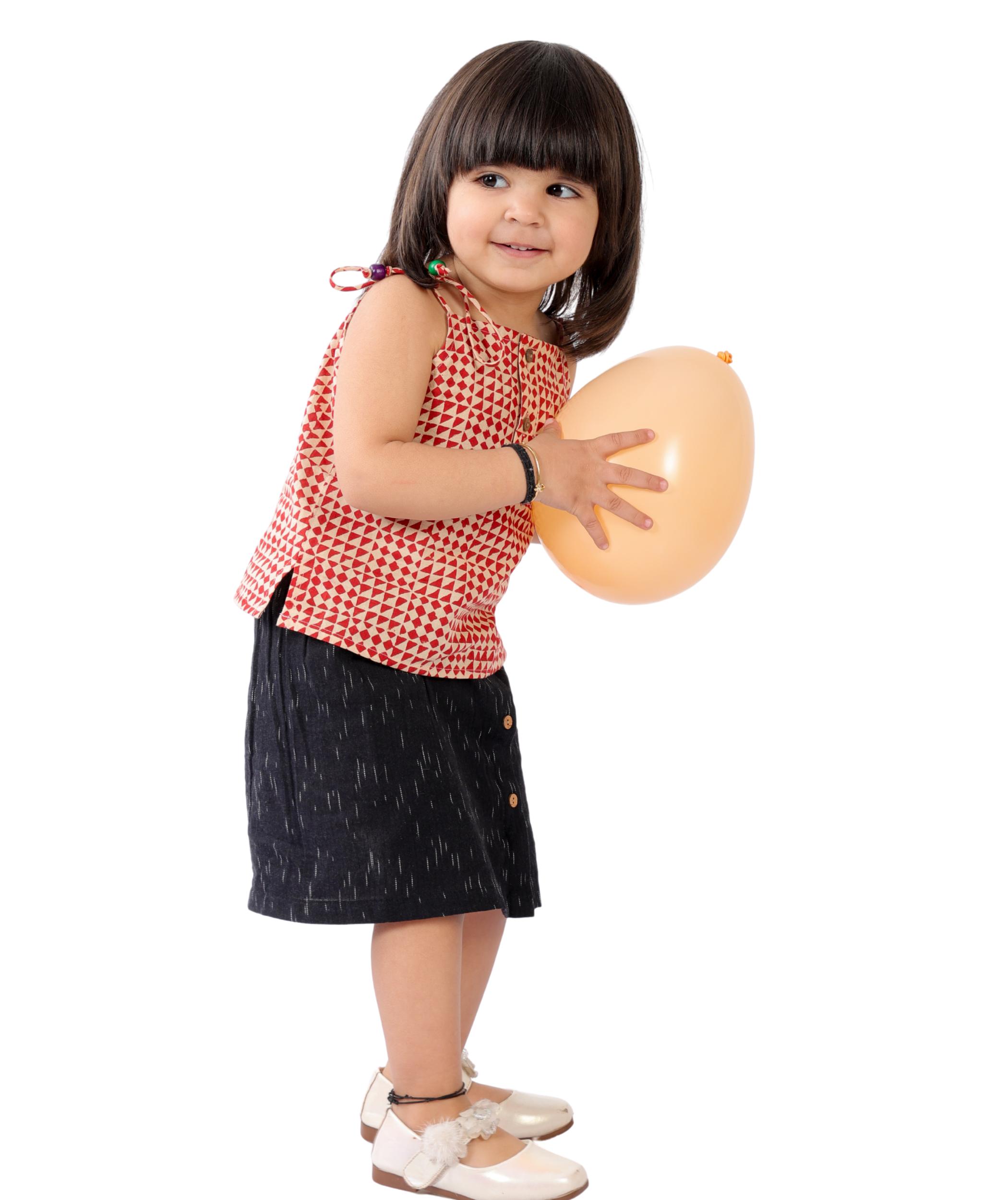 Baby girl wearing Tiny Bunnies red printed cotton top with black ikat skirt, shoulder tie party outfit